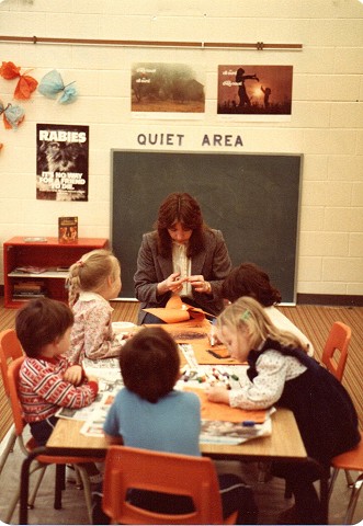 an old picture of an educator in a classroom with several children sitting around a table